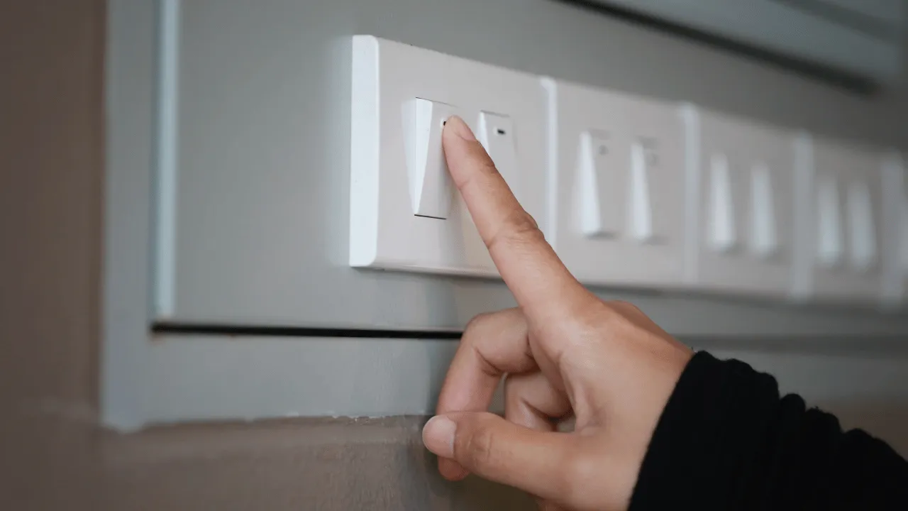 Persona encendiendo un interruptor de luz en una instalación eléctrica doméstica, representando el uso de interruptores para controlar el flujo de electricidad.