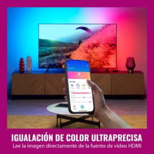 Persona sosteniendo un smartphone controlando los ajustes de color en la app WiZ frente a un televisor con luces dinámicas azul y roja.