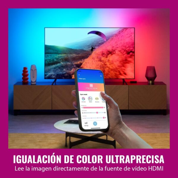 Persona sosteniendo un smartphone controlando los ajustes de color en la app WiZ frente a un televisor con luces dinámicas azul y roja.